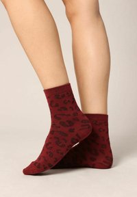 Chaussettes de cheville bordeaux avec un motif léopard noir, présentant une texture douce et des bords côtelés pour un ajustement sécurisé. Tissu finement tricoté.