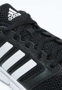 Černá sportovní bota s síťovinovým svrškem, zdobená bílými pruhy a černými tkaničkami. Pevná podešev s odpružením pro podporu a stabilitu.