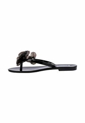 Black thong sandals featuring a glossy finish with a flower accent, flat sole, and minimalistic design. Made of synthetic material.