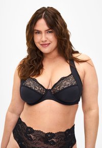 Black bra with lace detailing on the cups, structured shape, and wide straps. Features a smooth band and ornate lace accents on matching underwear.