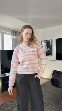 Camisola às riscas em cores pastel (rosa, azul, verde) com decote redondo e bainha canelada, combinada com calças pretas de perna larga.