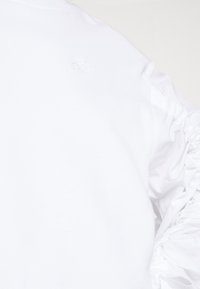 Vit långärmad skjorta med ett samlat texturerat mönster på  ärmarna och en liten präglad logotyp på bröstet. Mjuk bomullstyg.