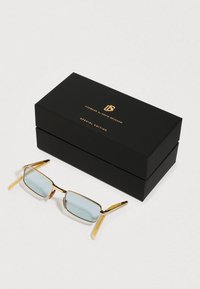 Crni pravokutni okvir za naočale s natpisom "Naočale od Davida Beckhama, posebna edicija" uz koje se nalaze naočale u pravokutnom obliku s zlatnim okvirom i plavim toniranim staklima.