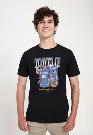 Jeune homme portant un T-shirt noir avec des serviettes bleues animées et le texte "Towelie" et "Je n'ai aucune idée de ce qui se passe."
