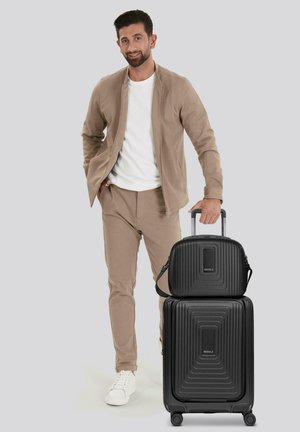 L'ensemble de valises rigides noires comprend une grande valise avec des rainures et un sac plus petit assorti. Texture lisse, équipé de roues et de poignées.