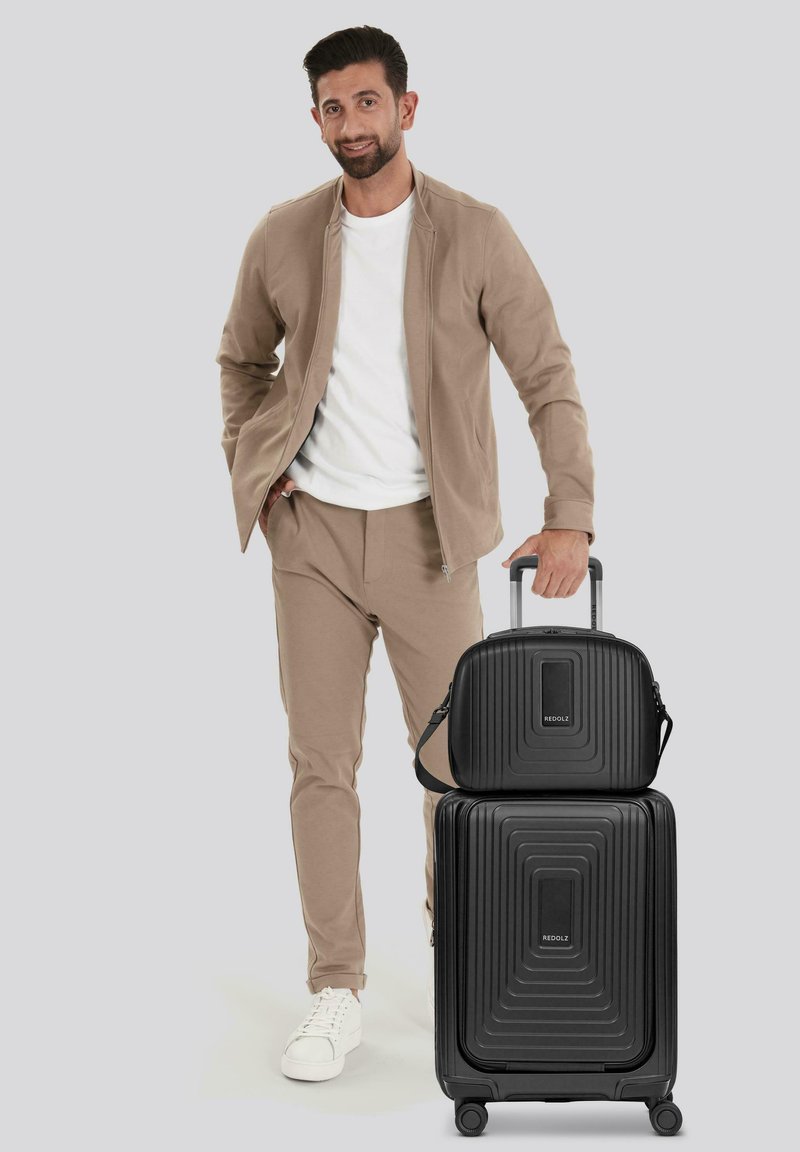 Zwart hard-shell bagageset, bestaande uit een grote koffer met groeven en een bijpassende kleinere tas. Glad textuur, uitgerust met wielen en handgrepen.