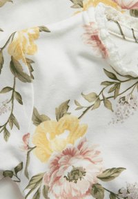 Blommigt tyg i vitt, med gula och rosa blommor samt gröna blad. Texturen är mjuk, med ett subtilt ribbat mönster.