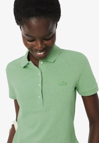 Polo vert en tissu texturé, avec un col et des manches courtes. Présente un logo brodé vert assorti sur la poitrine gauche.
