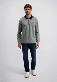 Langärmliges graues Poloshirt mit schwarzem Kragen, ausgestattet mit einer Brusttasche, kombiniert mit dunkelblauen Jeans und weißen Sneakern.