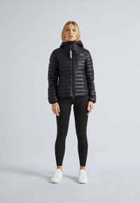 Svart puffjacka med huva, med dragkedja framtill, horisontellt kviltad design, kontrasterande vita dragkedjor och en smal passform, kombinerad med svarta leggings.