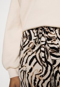Beige sweatshirt with puffed sleeves above black and beige tiger-striped pants featuring a tied waist. Soft fabric with a smooth texture.