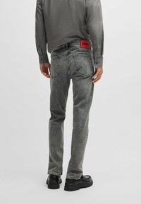 Jeans in denim grigio con una finitura sbiadita, caratterizzati da un'etichetta rossa sul retro. Abbinati a una maglietta a maniche lunghe grigia chiara e scarpe nere.