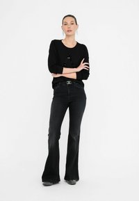 Top nero a maniche lunghe con un design di paillettes, abbinato a jeans a vita alta e a zampa in denim scuro; il modello indossa scarpe texture.