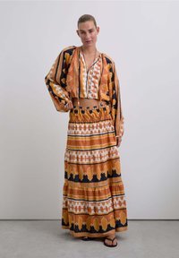 Ensemble en deux pièces comprenant un haut court à motifs orange et noir avec de larges manches et une jupe longue assortie à motifs géométriques.