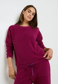Sweat-shirt en maille magenta avec un col rond et des manches côtelées, porté avec un pantalon assorti doté d'un cordon de serrage avec un motif à pois.