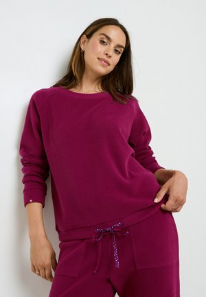 Felpa magenta a maglia con collo rotondo e maniche a costine, indossata con pantaloni coordinati dotati di coulisse con motivo a pois.