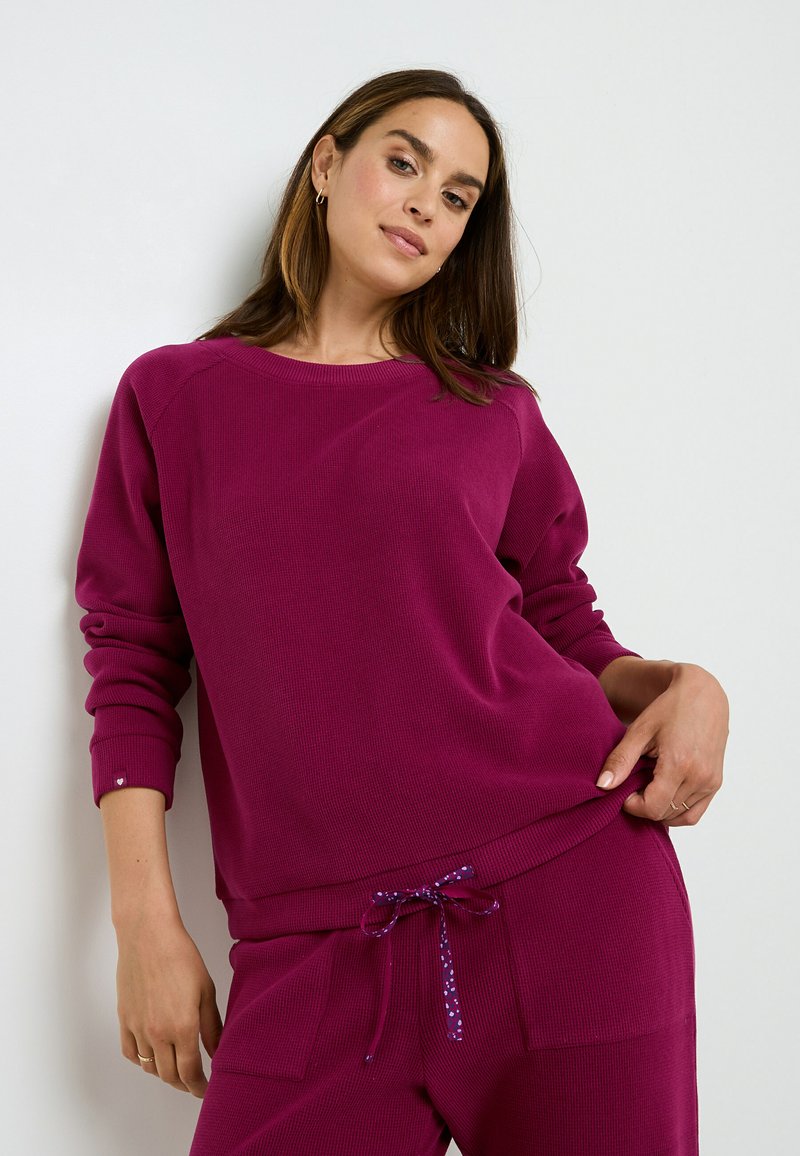 Sweat-shirt en maille magenta avec un col rond et des manches côtelées, porté avec un pantalon assorti doté d'un cordon de serrage avec un motif à pois.