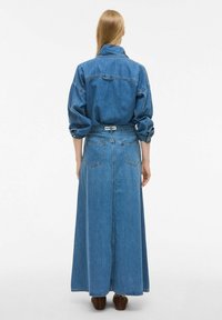 Denim obleka z dolgo, ohlapno silhueto. Svetlo modra barva, oversized zgornji del v stilu srajce, elastičen pas in gumbi na manšetah.