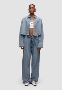 Giacca di jeans azzurro chiaro a cropped con colletto, abbinata a pantaloni di jeans a vita alta e dal taglio loose. Gli accessori includono una canotta bianca e delle scarpe.