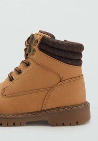 Botine bej cu un exterior din piele netedă, guler din fetru maro, sireturi contrastante și talpă din cauciuc rezistentă cu modele de aderență.