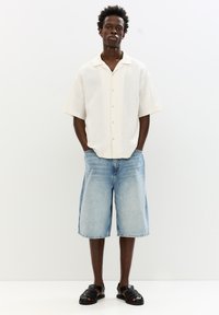 White short-sleeve button-up shirt with textured fabric, paired with light blue knee-length denim shorts and black woven sandals.