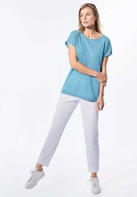 Lichtblauw kortemouwen shirt met een relaxte fit, gecombineerd met witte slim-fit broek en witte sneakers, tegen een minimale achtergrond.