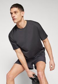 Mørkegrå treningsT-skjorte og shorts, begge i et glatt stoff. T-skjorten har rund hals og korte ermer, designet for komfort.