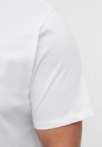 Hvid t-shirt med korte ærmer, glat tekstur, rund halsudskæring og en enkel kant. Stoffet virker let og åndbart.
