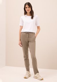 Lätta beige joggers med elastisk midja och snörning, ihop med en tajt vit t-shirt och beige sneakers, mot en neutral bakgrund.