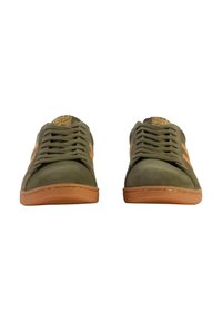 Sneakers in suede verde con suole, lacci e dettagli in gomma color beige. Presentano una superficie testurizzata e un logo sulla linguetta.