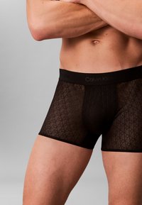 Czarne bokserki Calvin Klein z geometrycznym mesh wzorem, elastycznym paskiem w talii oraz przewiewnym materiałem dla komfortu i dopasowania.