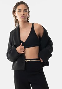 Musta bleiseri mustan ribbed bralette'n päällä, yhdistettynä korkeavyötäröisiin mustiin housuihin ja kultaisella yksityiskohdalla varustettuun vyöhön, jossa on solmu yksityiskohtana.