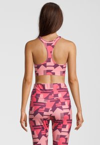 Sujetador deportivo rosa con un diseño de espalda corredora, que presenta un patrón geométrico en tonos más oscuros de rosa y púrpura. Combinado con leggings de talle alto a juego.