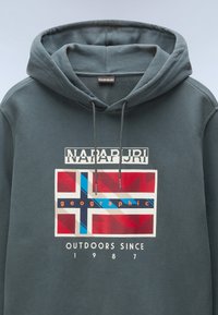 Sudadera con capucha en gris oscuro, con un diseño gráfico que presenta una bandera estilizada y el texto "NAPAPIJRI" y "OUTDOORS SINCE 1987" en blanco.