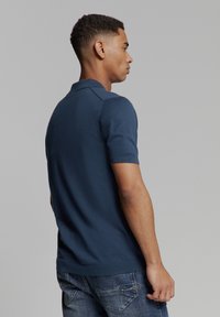 Marineblauwe polo met korte mouwen en een klassieke kraag, gemaakt van gebreide stof, met een rechte zoom en subtiele schouderdetails.