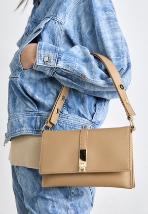 Beige leather handbag with a rectangular shape, featuring a gold-tone clasp closure and a detachable strap, worn with blue denim jacket.