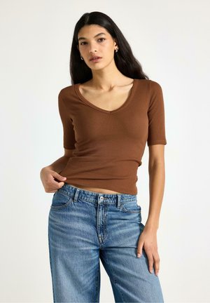 Brun kortærmet, ribbet top med V-udskæring, kombineret med lyseblå jeans med høj talje. Glat tekstur, tætsiddende silhuet.