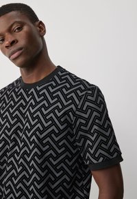 Sort kortærmet skjorte med geometrisk mønster og hævet tekstur. Ensfarvet sort rund halsudskæring og ærmekanter.