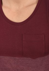 Burgundy színű ujjatlan felső, kerek nyakkivágással és zsebbel. Kényelmes pamut keverékből készült, sima tapintással. Színblokkos kialakítással a szegélyen.