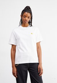 Witte katoen T-shirt met een ronde hals, korte mouwen en een klein, geel logo op de borst. Gekocht bij donkere jeans met een kettingdetail.