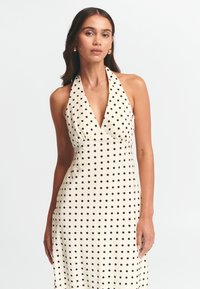 Polka-täpid dress, millel on kreemja taustaga mustad täpid, kaeluse disain ja sobiv siluett, mis voolab õrnalt allapoole.