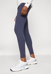 Marina blå leggings i stretchigt material med smal passform. Kombinerad med vita träningsskor, som har mesh och detaljer i ljusblått.