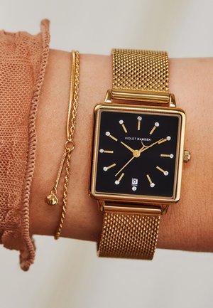 Montre avec bracelet en maille dorée, dotée d'un cadran carré noir, de repères horaires dorés et d'accents argentés. Comprend un bracelet délicat avec un petit pendant.