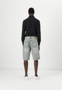 Camiseta negra de manga larga y pantalones cortos de mezclilla claros, con bolsillos traseros y una etiqueta, complementados con zapatillas blancas.