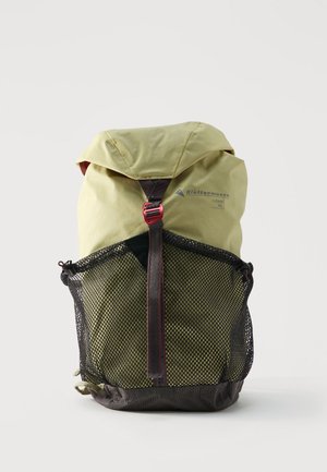 Rucsac verde deschis Klättermusen Fjorm de 18L, cu buzunar frontal din plasă neagră și curea cu cataramă roșie, prezentat pe un fundal alb.