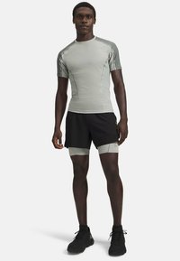 Sportliches Outfit mit einem grauen Kurzarm-Oberteil aus strukturiertem Stoff und schwarzen Shorts mit grauen Akzenten, kombiniert mit schwarzen Sportschuhen.