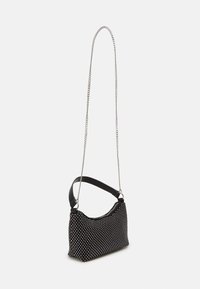 Sac à bandoulière en tissu noir avec des clous argentés, fermeture éclair, courte sangle noire et longue chaîne argentée.