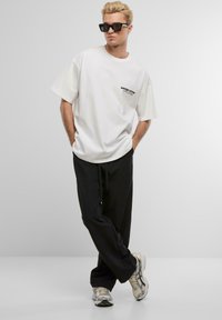 White cotton t-shirt with printed text, paired with black loose-fitting pants. Accessories include sunglasses and gray sneakers.