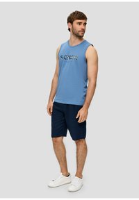Chemise sans manches bleu clair avec un imprimé graphique, associée à un short navy foncé et des baskets blanches. Design athlétique décontracté.