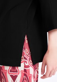 Top nero con maniche corte, fessura laterale che rivela un tessuto a fantasia rosa e rosso. Metti in risalto i colori e le texture a contrasto.